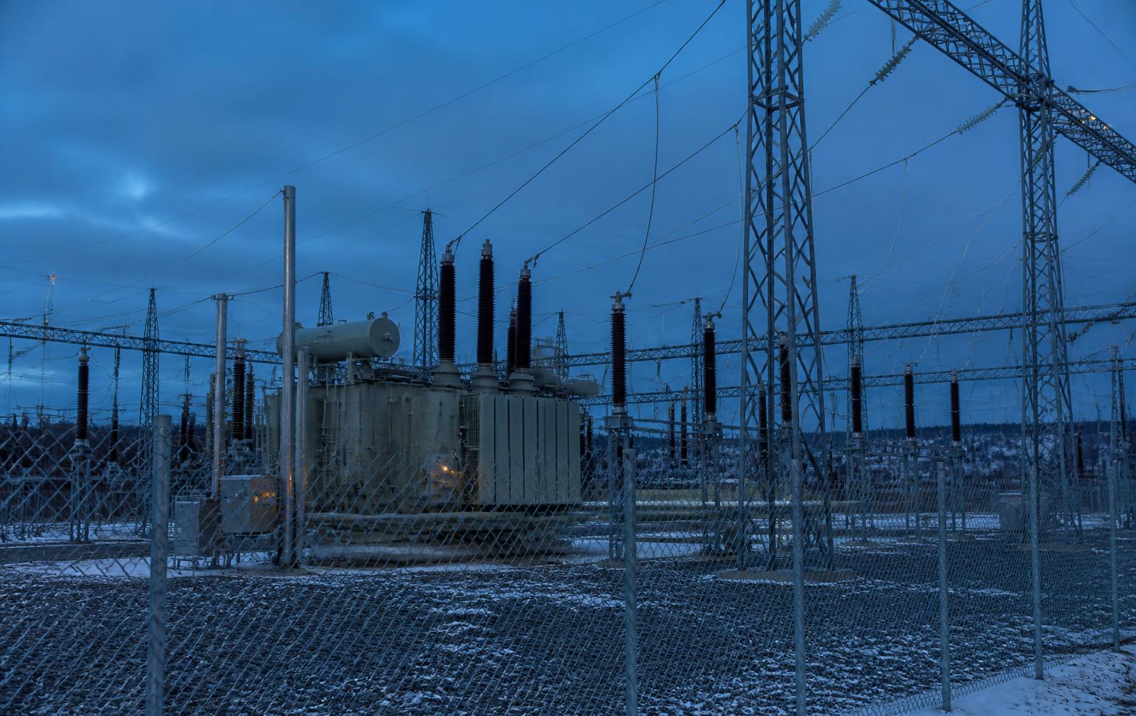 Nordic high-voltage substation behind a security fence at blue hour