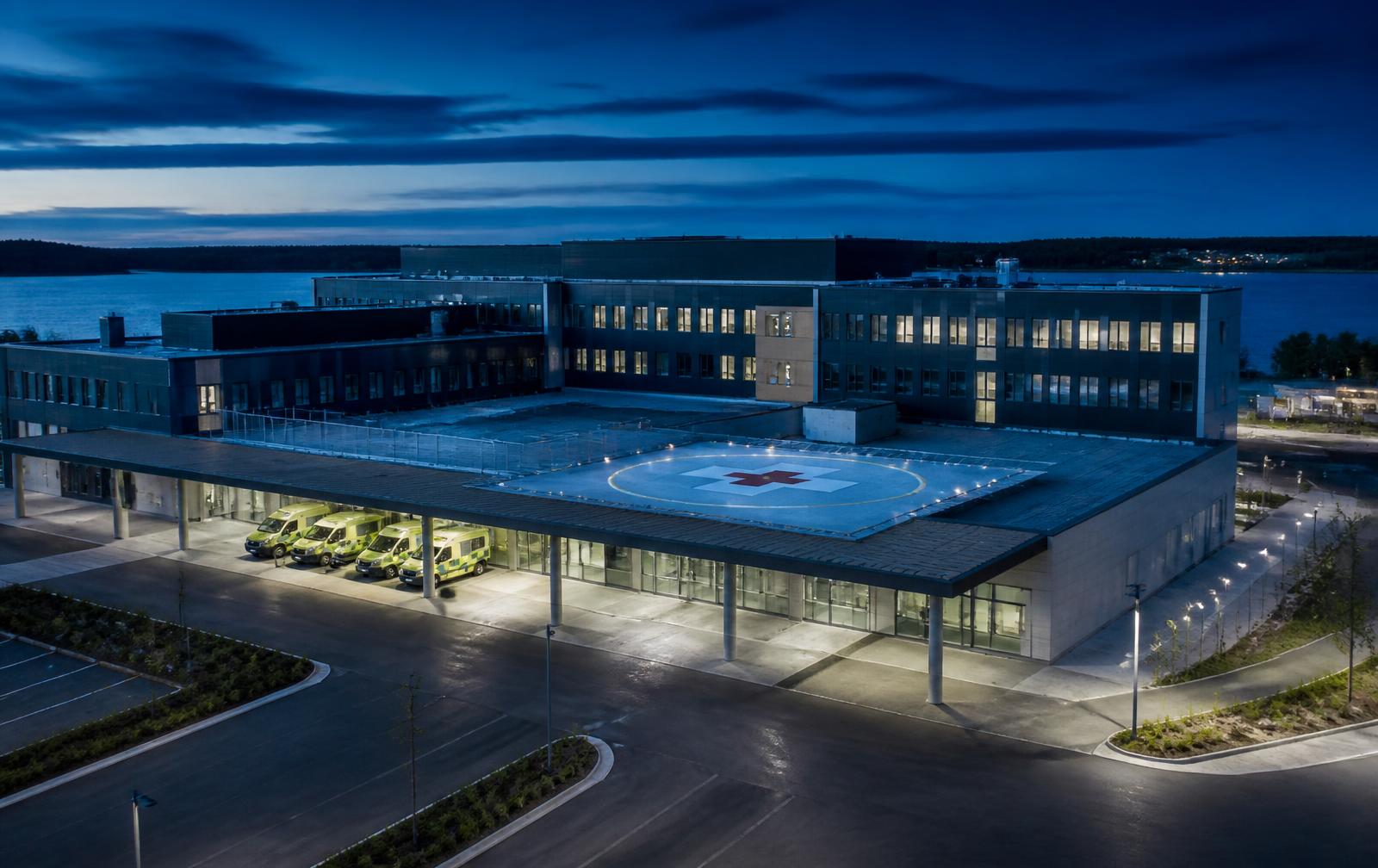 Modern hospital campus with ambulance bay and rooftop helipad at dusk