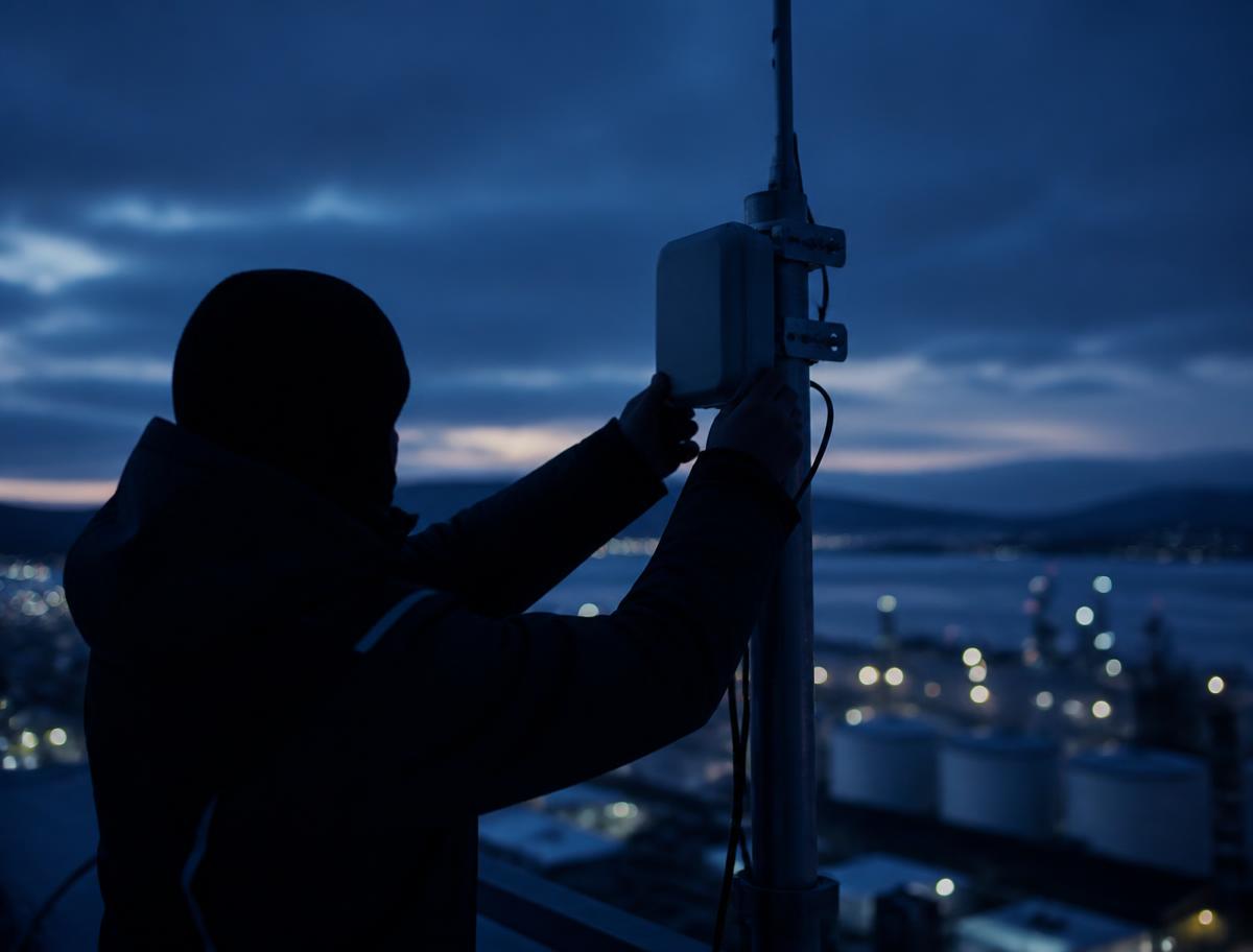 Technician mounting a compact sensing node on a rooftop mast